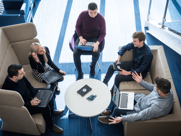 a group of Benamic employees sitting on couches on there laptops having a work meeting