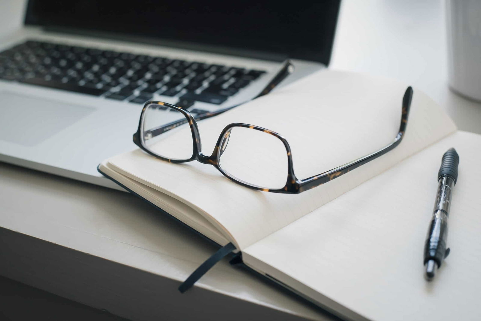 Glasses lying on a notebook at an office desk beside laptop