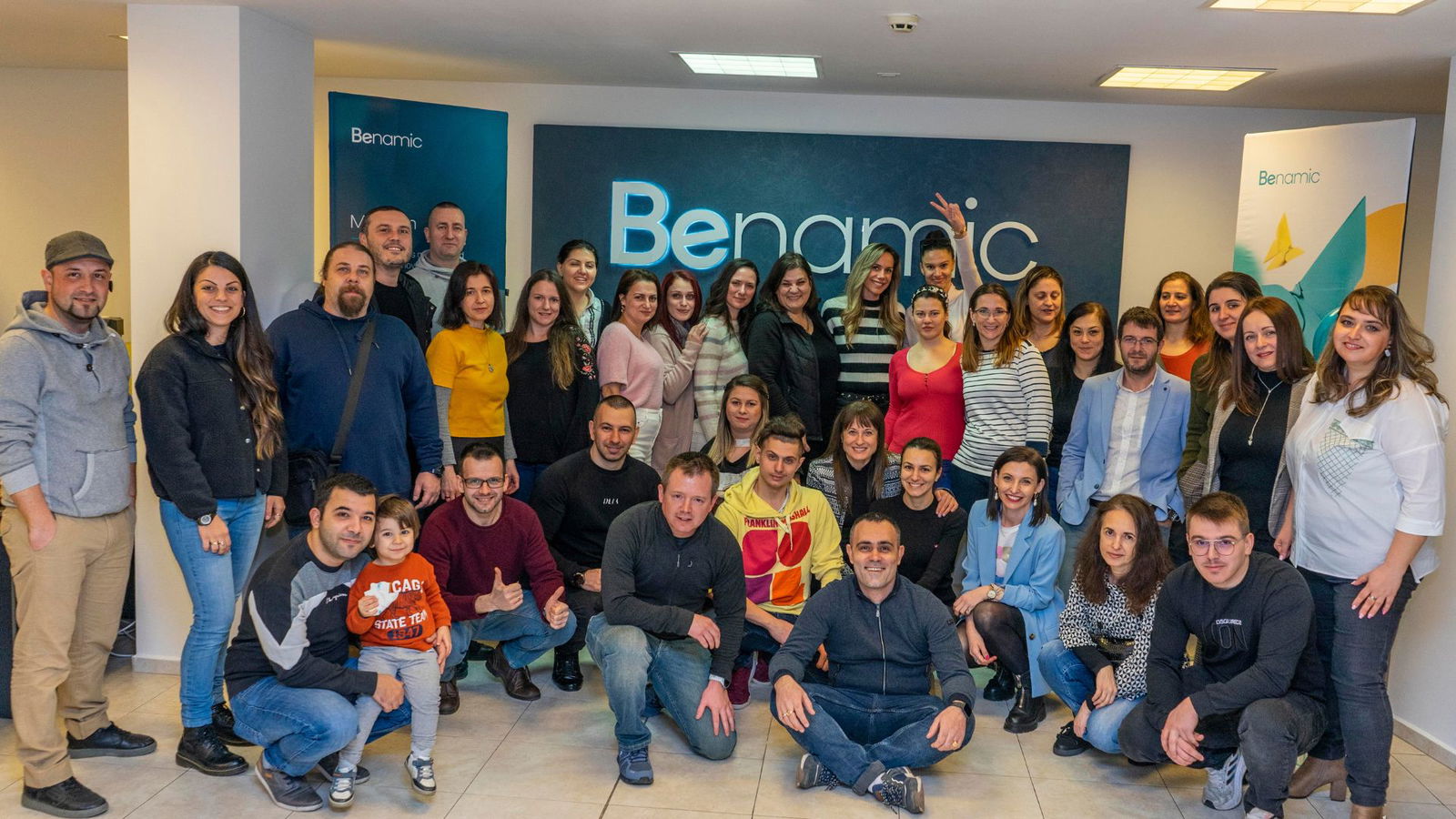 A group of all Benamic employees celebrating in front of Benamic sign at New Hybrid Office Space Party.