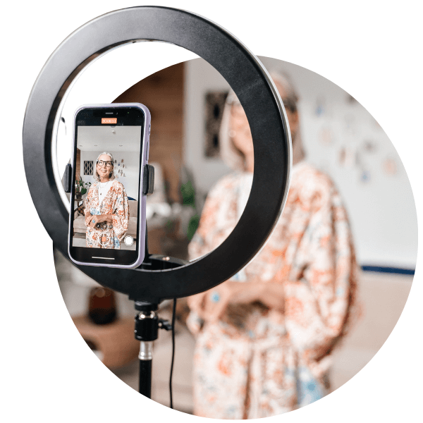 a senior woman taking a video on herself and looking at her phone attached to a ringlight