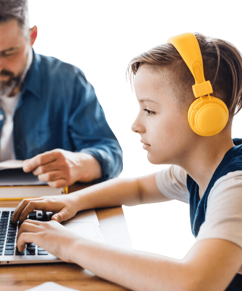 a young boy at a table with his dad typing on his computer with headphones on