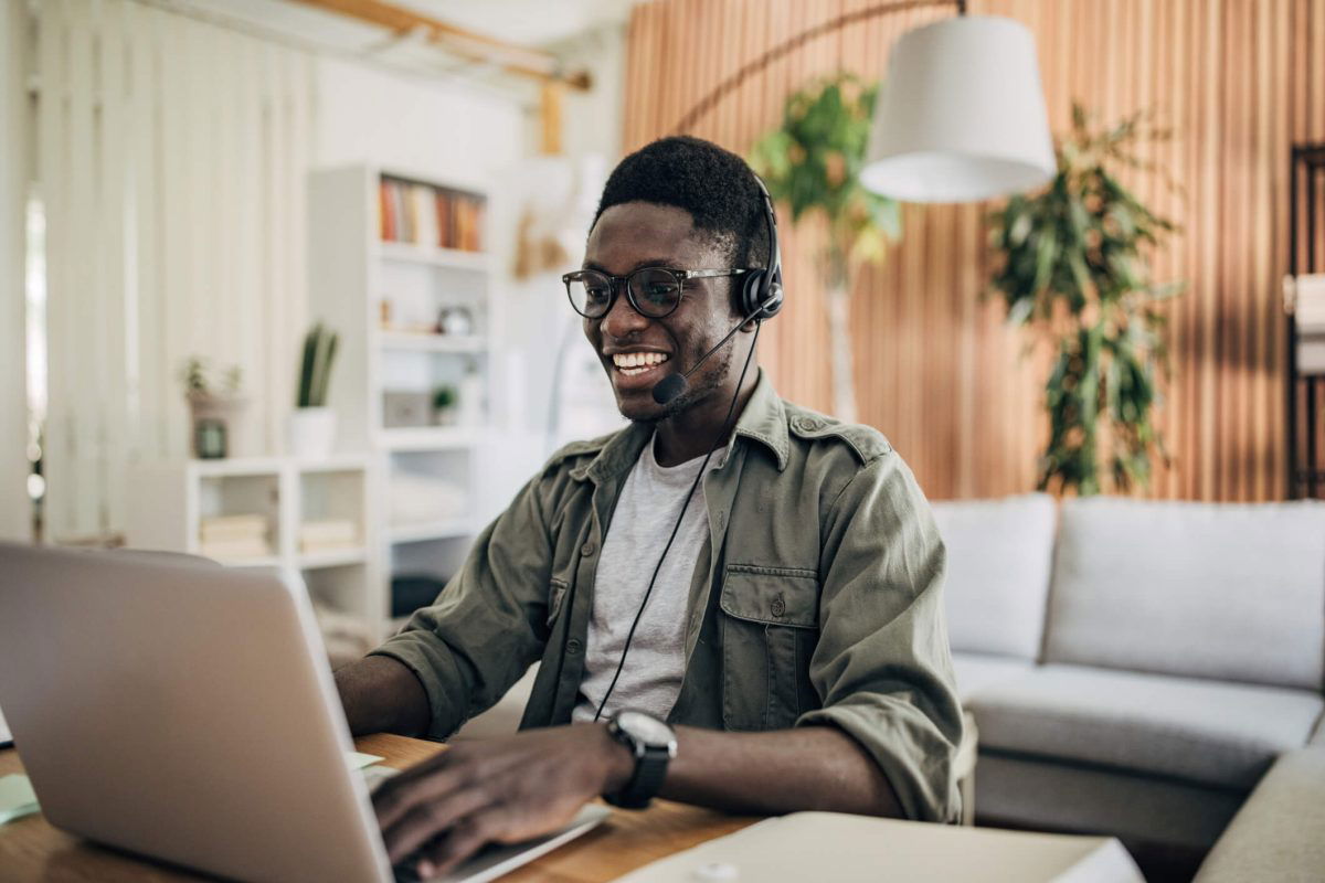 a man with a headset on their laptop in their home having a video call and e learning