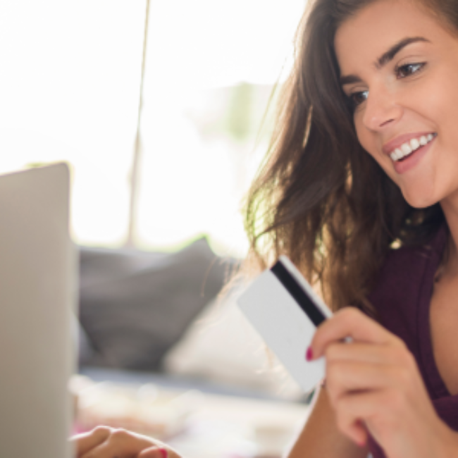 Woman smiling in front of laptop with credit card in her hands